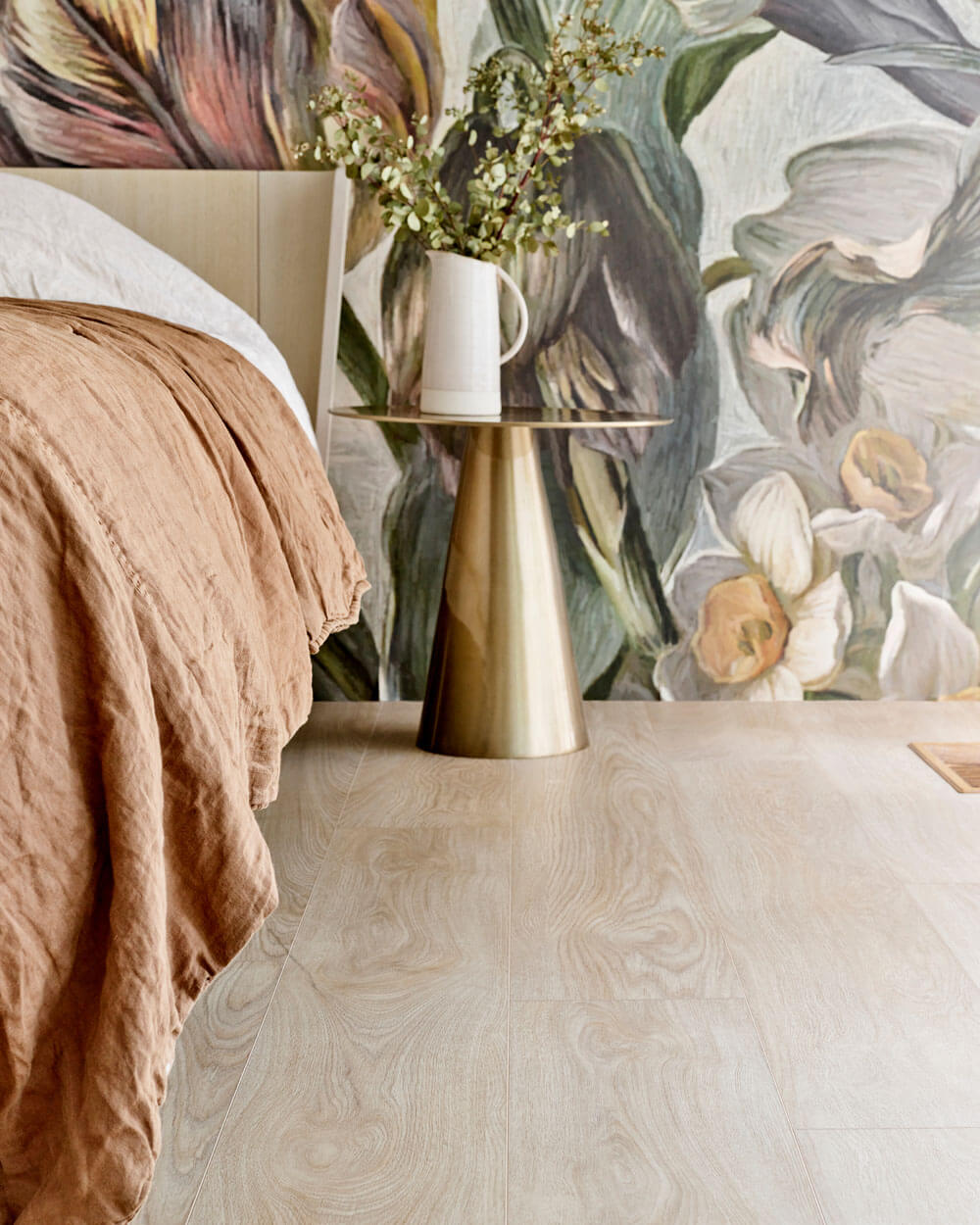 Interior of a bedroom with a bed against a wall with floral wallpaper. The floor shown is Moduleo LayRed Laurel Oak 51230 Embossed luxury vinyl flooring.